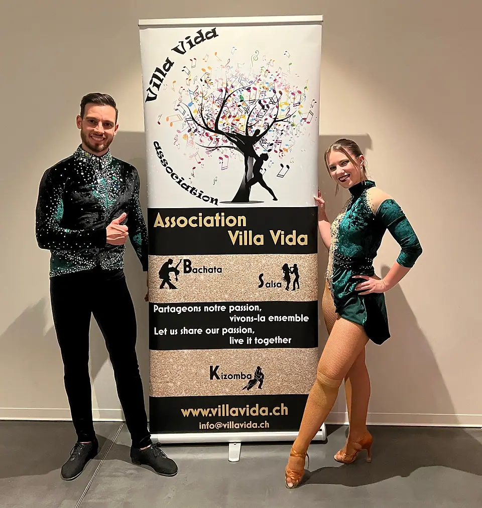 Un danseur et une danseuse en costumes de scène verts, de part et d’autre du roll-up Villa Vida ; au bas du roll-up, l’adresse info@villavida.ch.