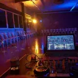 Une table de mixage et un ordinateur portable face à une salle vide, éclairée en bleu et orange.
