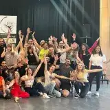 Photo de groupe : une cinquantaine de danseuses et danseurs, bras levés, devant le roll-up.