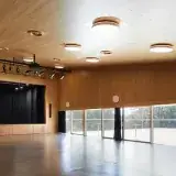 La grande salle des Utins à Echandens : parquet sombre, plafond en bois, scène aux rideaux noirs.
